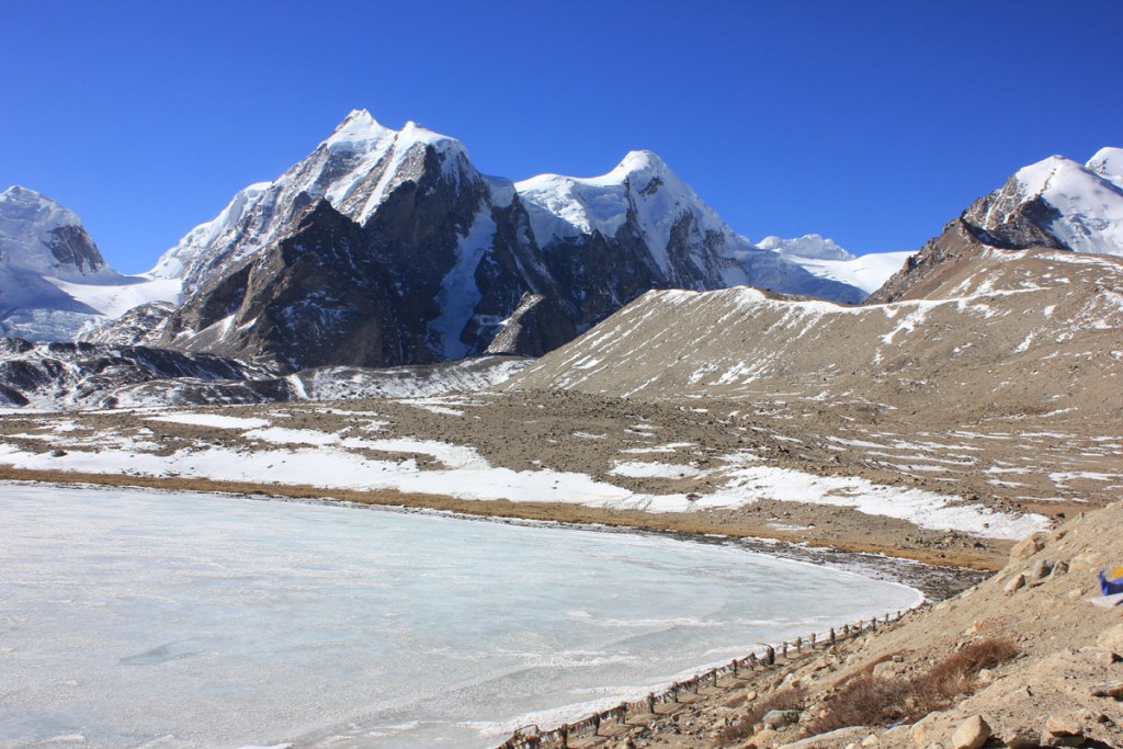 Frozen Gurudongmar lake in sikkim with barren brown desert around and shorter himalayan mountains