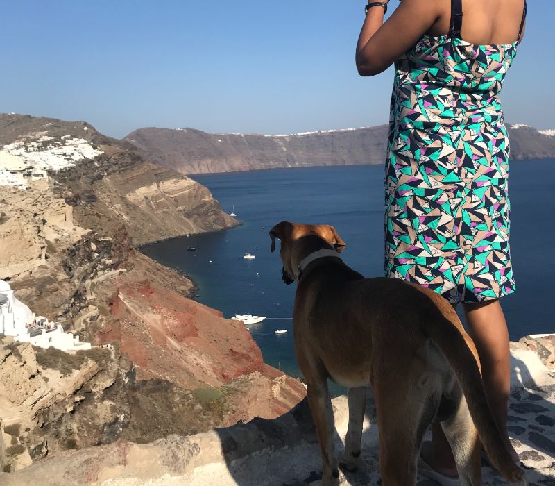 Woman traveller wearing skirt standing by the cliffside overlooking Santorini sea in Greece