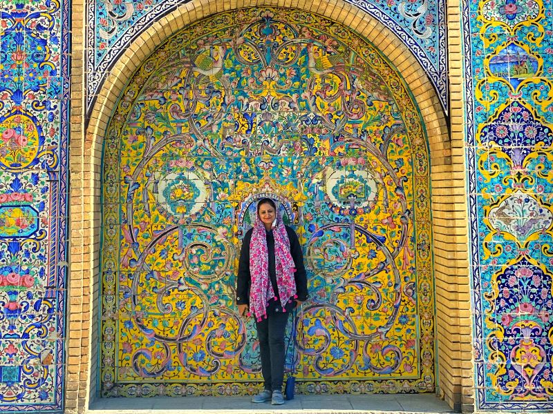 Woman wearing hijab in Iran standing in front of colourful glazed tile cladded wall in Tehran