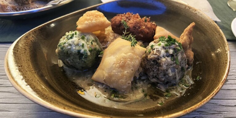 Dish with mixed appetizers including dumplings, veg balls , and fritters garnished with herbs on a brown ceramic plate