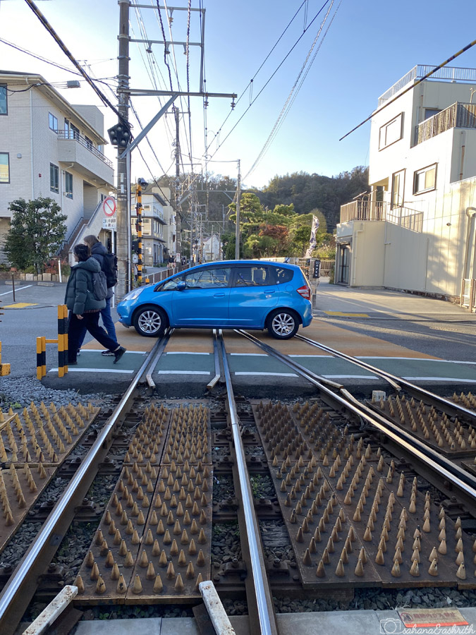 blue car crossing railway tracks in town centre at Kamakura