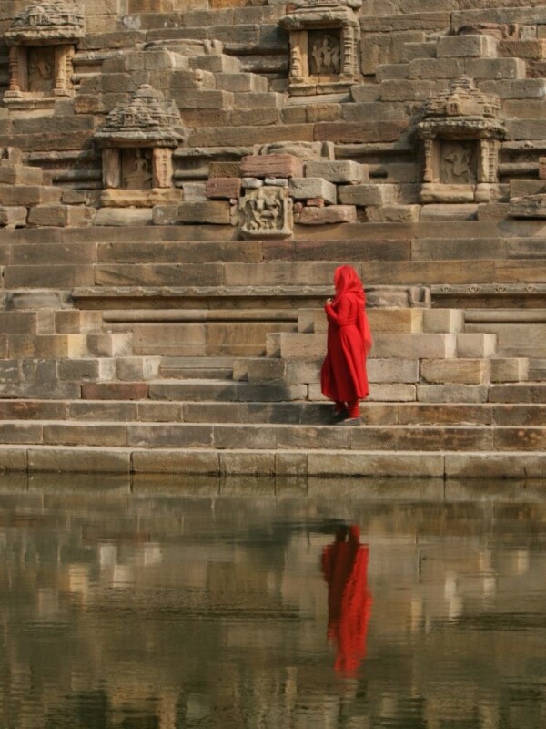 woman in salwar kameez with dupatta over head walking beside a stepwell filled with water in gujarat