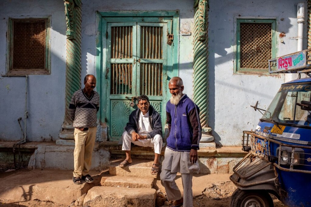 3 Gujarati old men in shirt and paijama sitting and standing in front of an old house by the streetside