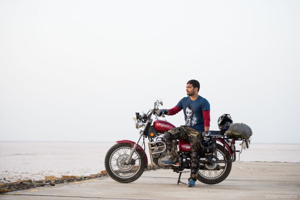 MAN SITTING ON BULLET BIKE ON THE WHITE SALT FLATS OF RANN OF KUTCH IN GUJARAT