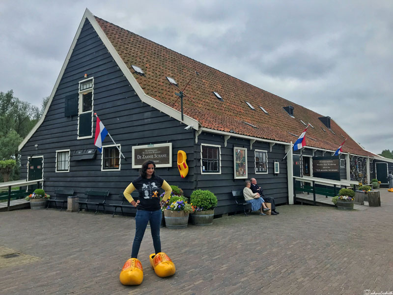 sahana standing in front of traditional dutch house wearing a giant wooden clog