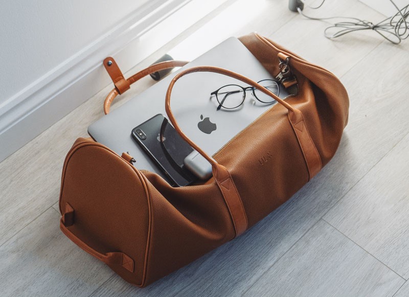 leather handbag on the floor with zip open fitting a laptop, phone and spectacles