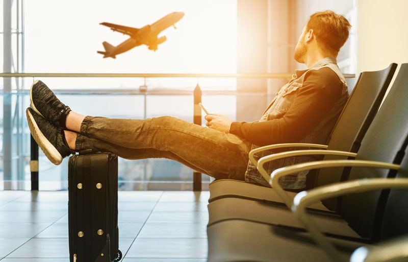 man sitting on a chair with legs stretched beside window during sunset watching an aeroplane taking off in airport