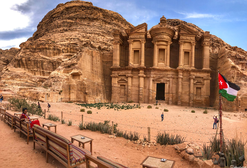 indian girl sitting on a bench in front of monastery in petra, jordan