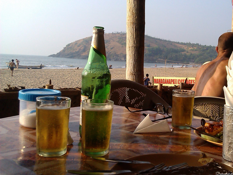 india travel guide showing 2 glass of beer and a bottle on table in a shack beside ocean in Gokarna
