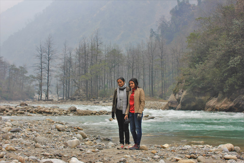 Two Indian women standing beside the Teesta River in Sikkim, surrounded by stunning scenery during winter.