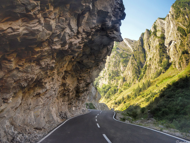 carved rock bending above asphalt road beside cliff overlooking water and green mountains in Uttarkhand