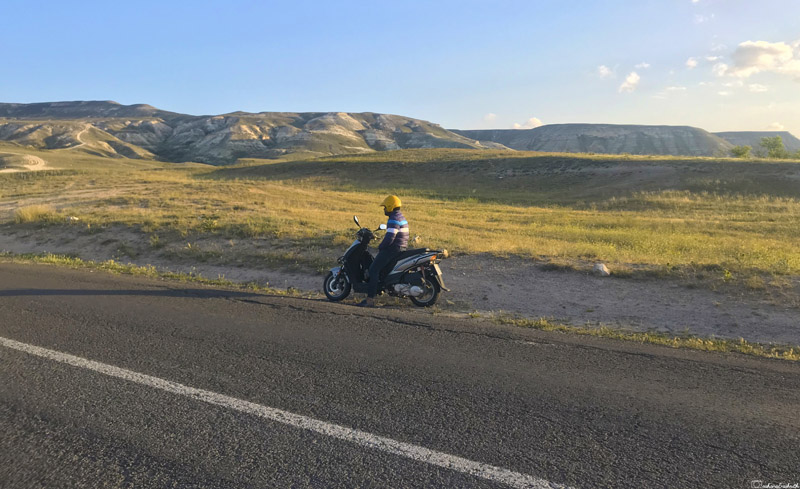 a man wearing helmet on scooter in an isolated meadows with short mountains in cappadocia