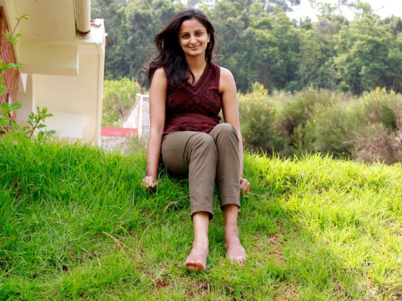 Sahana seated on a grass lawn, wearing a sleeveless top and slim bottoms.