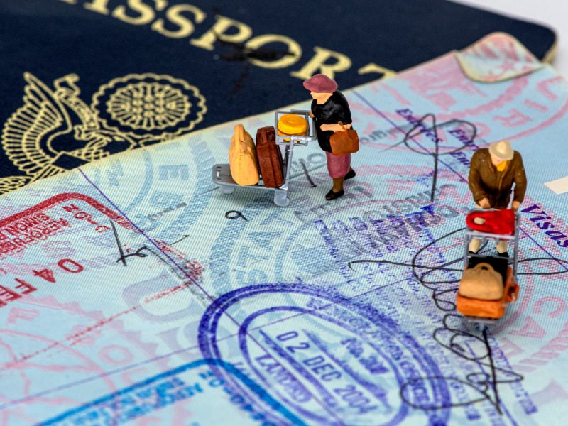 a passport page with multiple stamps and two miniature statue of tourists pushing trolley on the pages