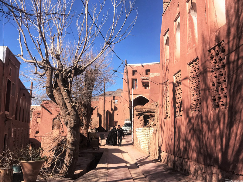 woman in burqa and a man walking in the narrow alley of abyaneh red adobe village houses