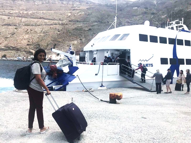 vacaywork author sahana holding a trolley standing at Thira port beside a "sea jet ferry"