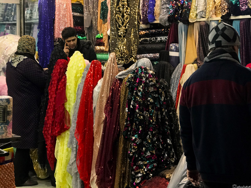 Shopkeeper at his store selling glamorous fabrics, engaging in conversation with customers
