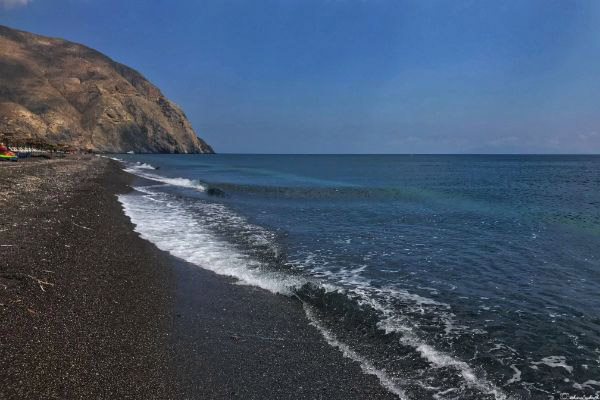 gentle waves of the aegean sea meeting the black sands and rocky mountains in perissa