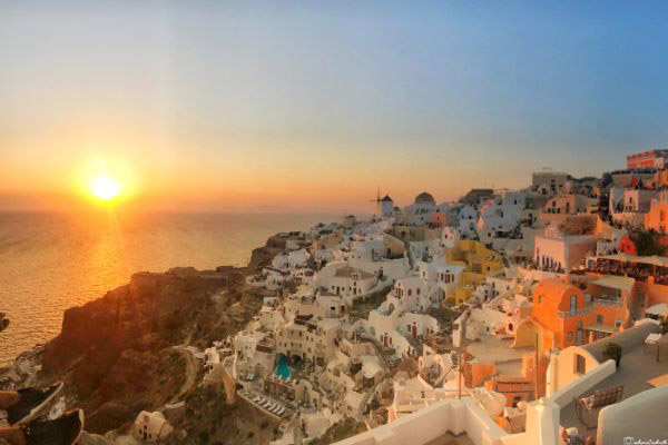 Colorful cube houses and windmills on a hill overlooking the glowing Aegean Sea at sunset in Oia