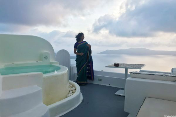 Author from Vacaywork donning an Ilkal saree, standing beside a cave pool at a luxurious resort with a view of the Caldera