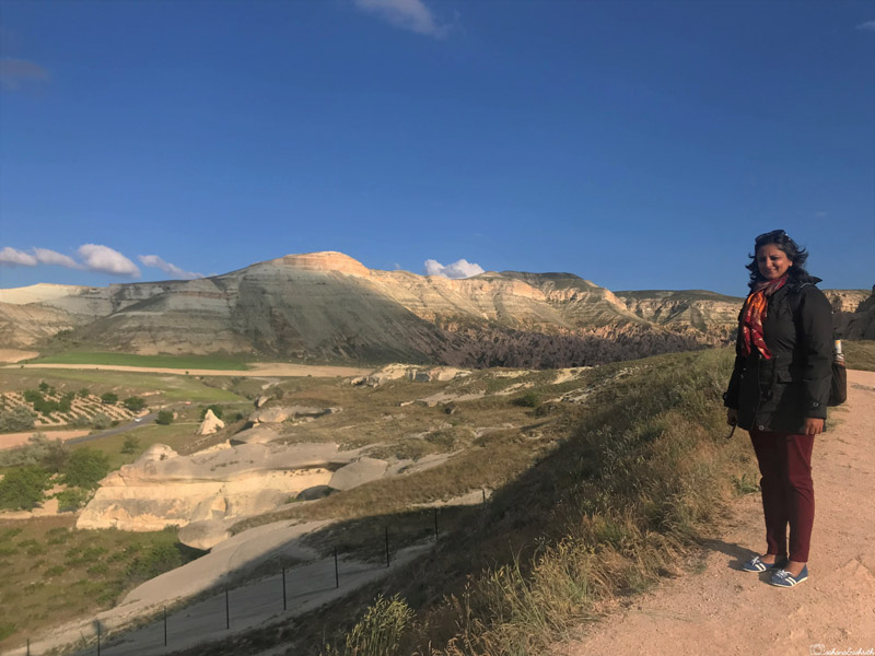 vacaywork author sahana standing on hill beside cliff and lime formations on hills behind her in cappadocia