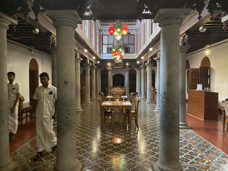 Two men in veshti walking on 120-year-old, beautifully designed Atthangudi tile flooring in the dining hall of the Heritage Hotel.