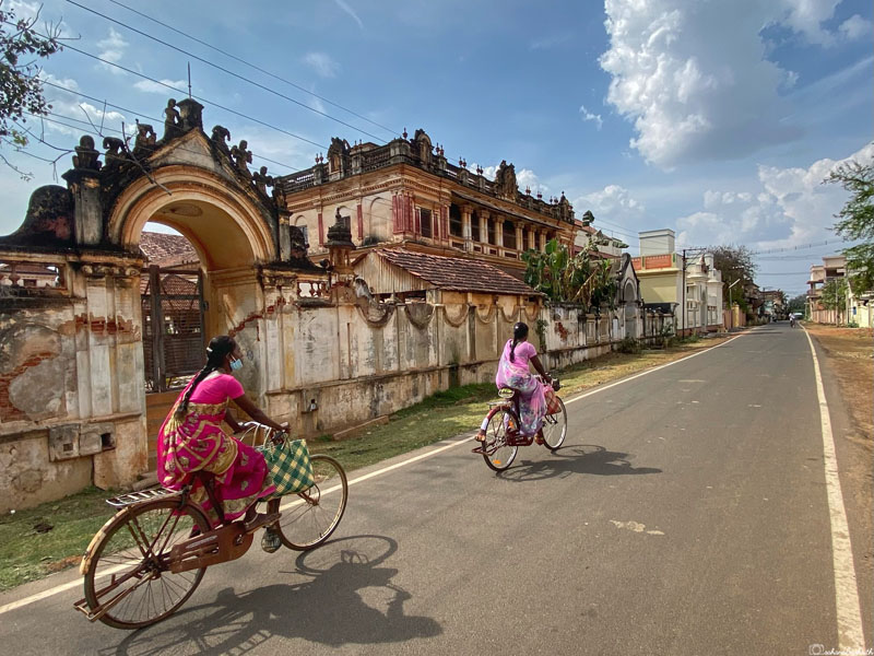 two woman in saree on bicycles beside abandoned chettinad mansions in kanadukathan