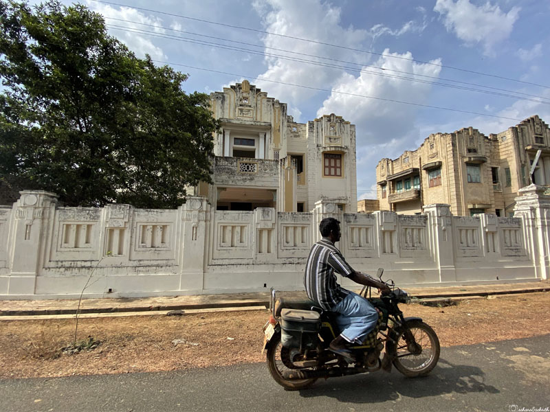 man on bike on the move on kanadukathan street in front of two twin abandoned chettinad mansions