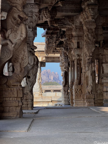 Sky visible between highly detailed, carved columns with yalis on either side of a pavilion at Vijaya Vittala Temple