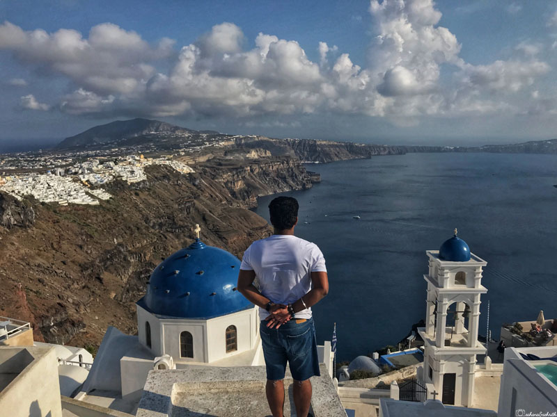 vacaywork author ashrith standing at the cliffside of caldera between two blue domes watching aegean sea in santorini