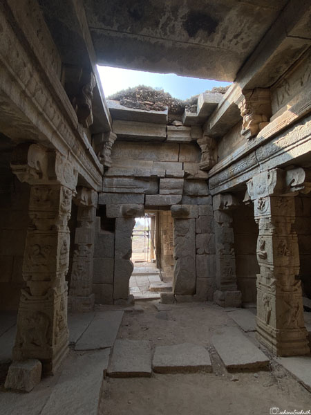 Open roof above with light casting onto partially mud-covered stone flooring, surrounded by carved stone columns with detailed relief sculptures at vaishnava temple