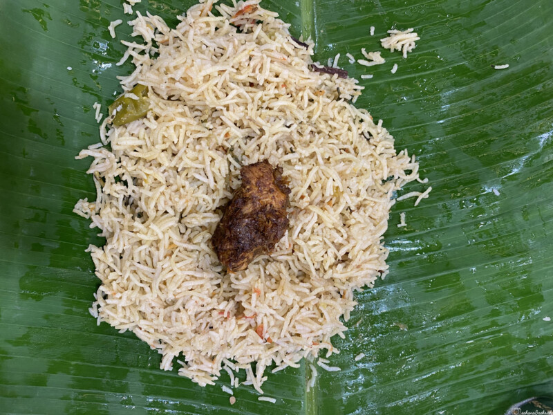 A serving of biryani with a piece of meat placed on a banana leaf