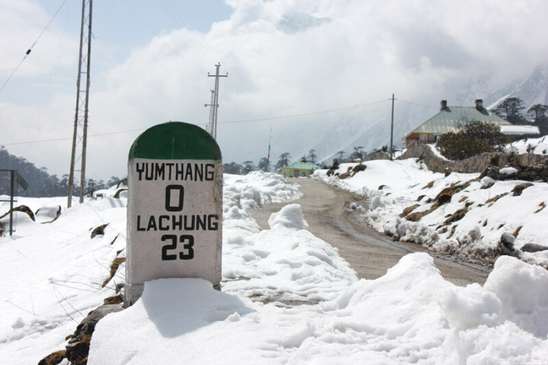 A milestone at Yumthang Valley in North Sikkim indicating a distance of 23 km to Lachung, with the snow-covered road and surrounding snowy landscape visible