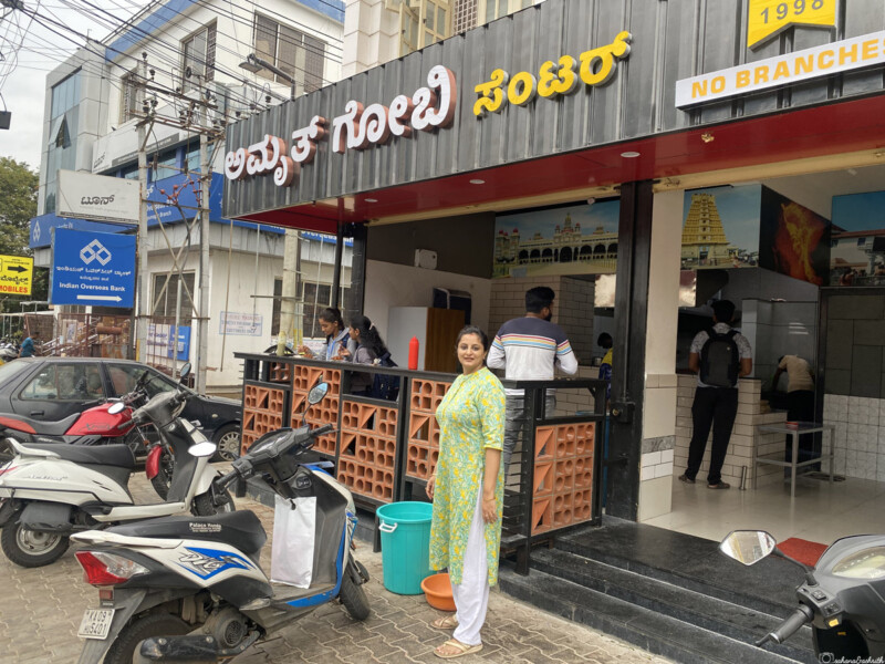 The entrance of Amruth Gobi Centre with a woman standing outside, located in a busy street.