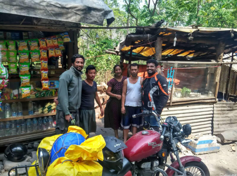 Two motorcyclists, pose for a photo with local sikkimese family in front of a roadside shop with various products.