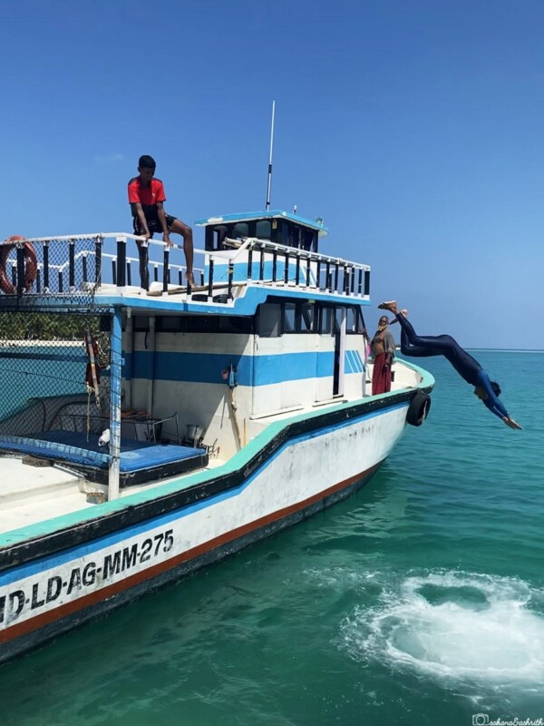 A person jumps off a boat into the sea while another person watches from the deck of fishing boat