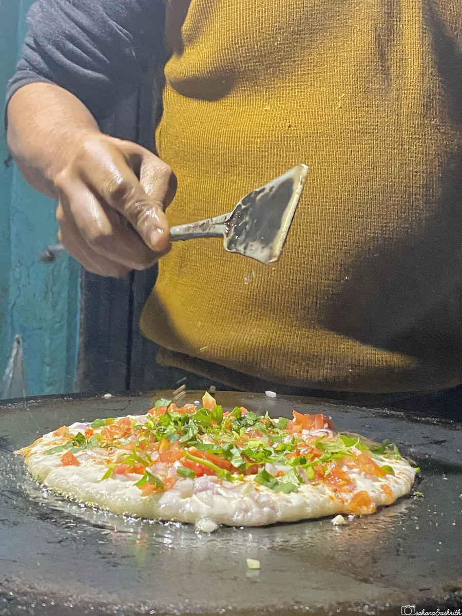 A close-up of a vendor making a dosa with fresh vegetables on a tawa in Varanasi.
