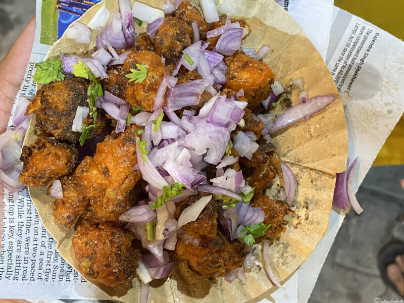 A plate of gobi manchurian pieces garnished with chopped onions and coriander, served on a paper plate