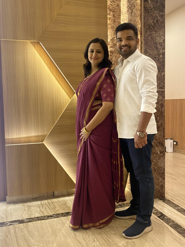 Man in a white shirt and woman in a maroon sari standing together indoors of a hotel lobby