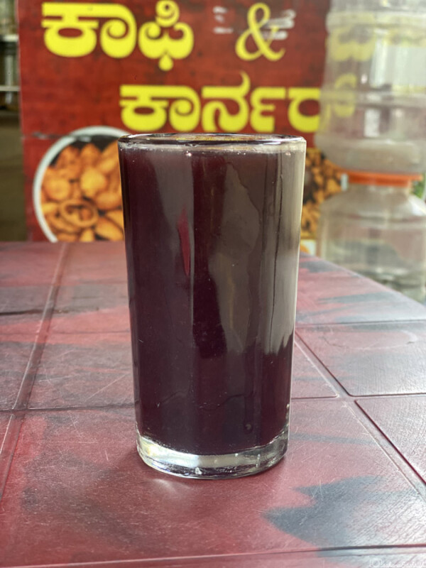 A glass of dark purple grape juice placed on a table with a red background.