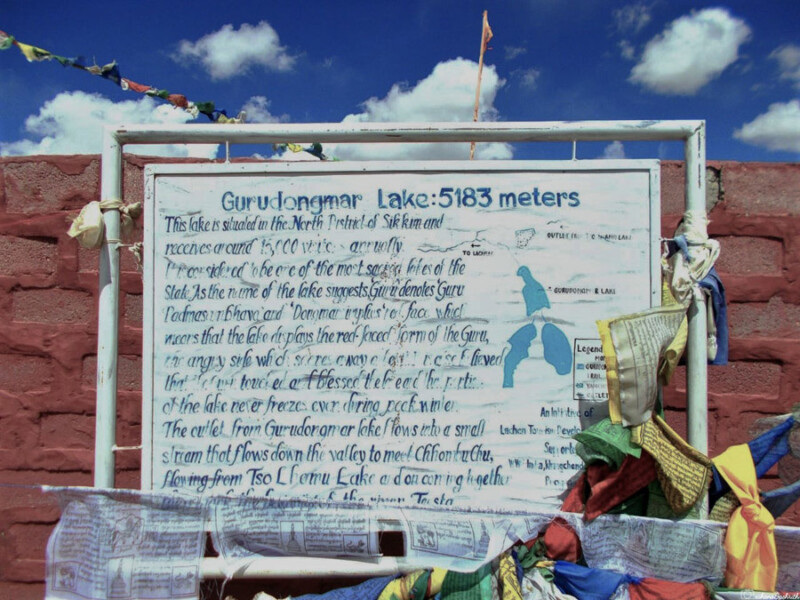 An informational sign about Gurudongmar Lake at an elevation of 5183 meters, adorned with colourful prayer flags