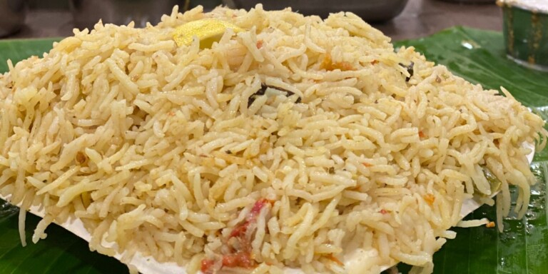 Close-up of a plate of biryani served on a banana leaf with visible spices and pieces of vegetables.