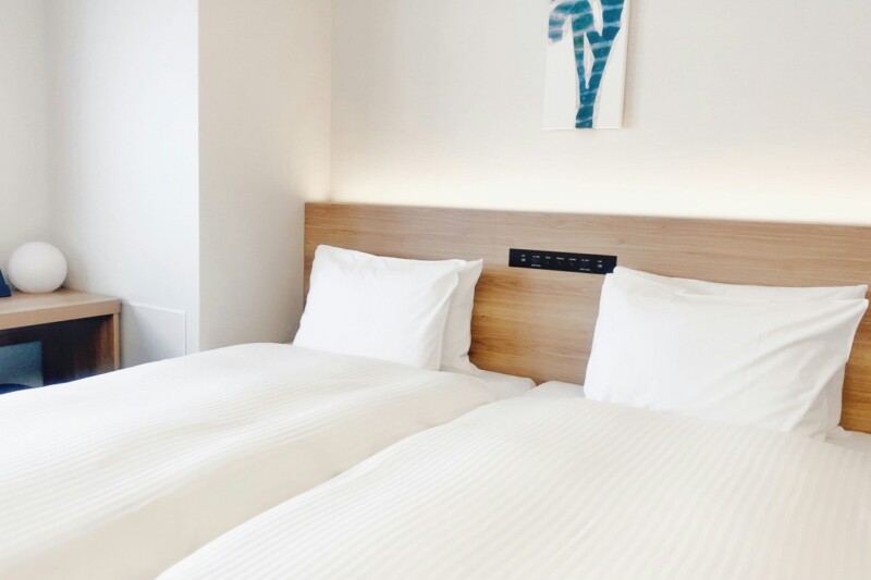 Minimalist hotel room with two single beds and white linens.