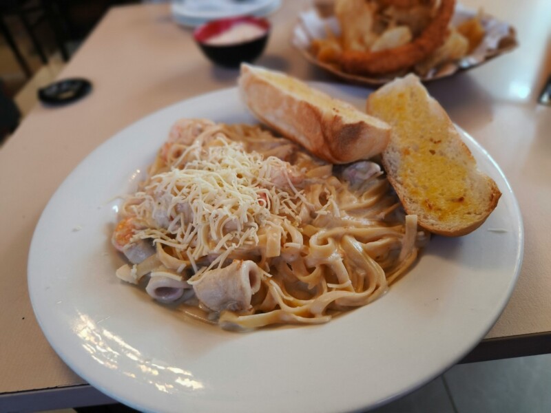 A plate of creamy pasta topped with grated cheese and served with a slice of garlic bread