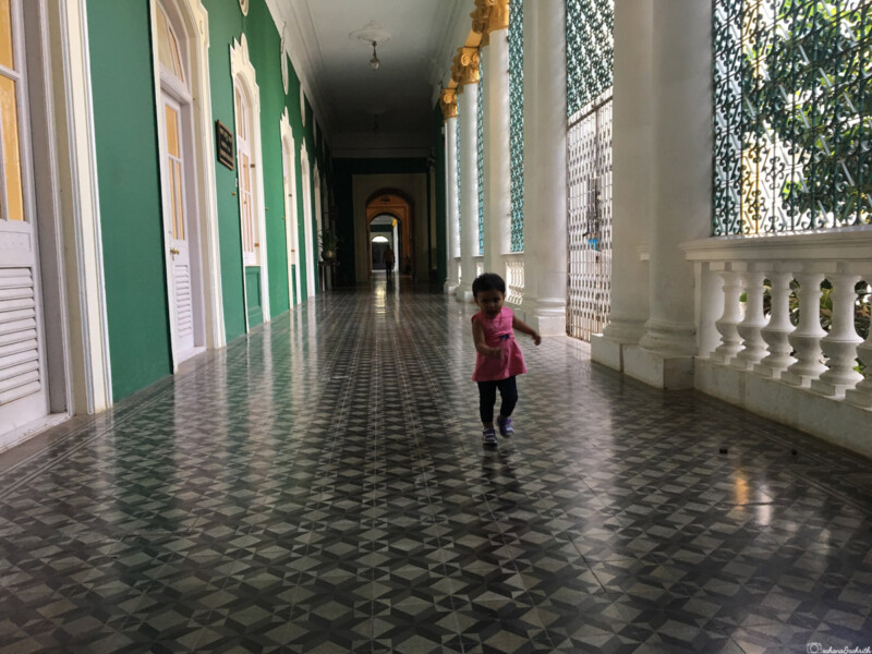 Toddler walking down a long hallway with patterned tiles and green walls at Lalitha Mahal Palace