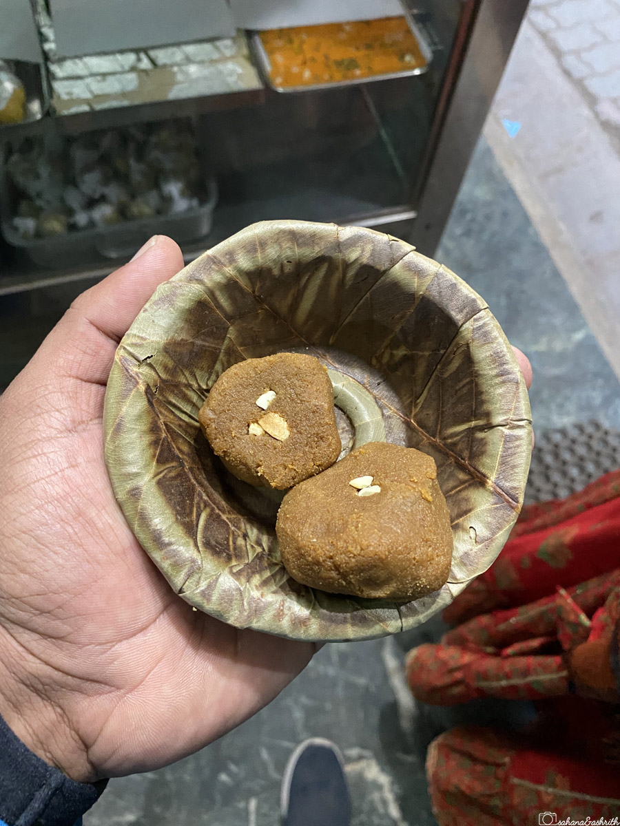 A plate with two pieces of Varanasi's famous Laal Peda, a sweet made from khoya and garnished with nuts, served in a leaf bowl.