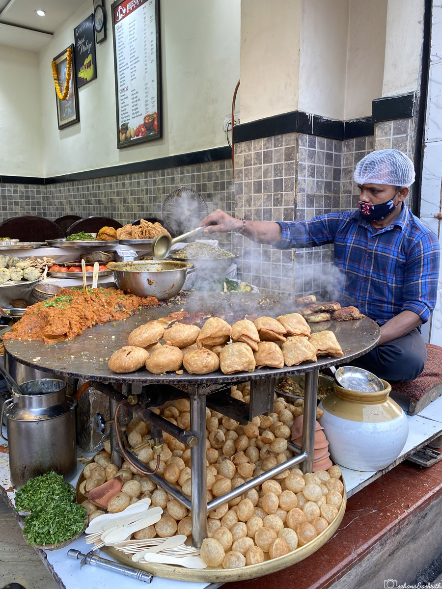 A vendor cooking various snacks on a large tawa at a street food stall in Varanasi