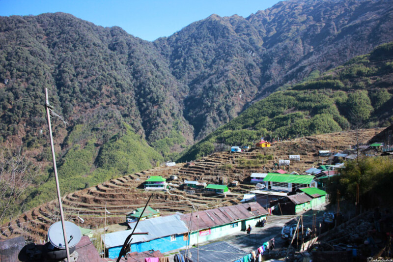 : A picturesque village in Sikkim, featuring terraced fields and colourful houses nestled in a valley surrounded by dense green hills.