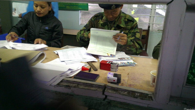 Two Sikkimese officials AT government of sikkim home department diligently process paperwork at a busy checkpoint, surrounded by documents and stamps