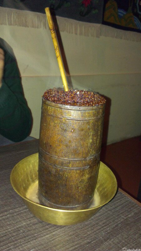 A traditional wooden container filled with fermented millet, with a straw sticking out, placed in a brass bowl